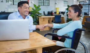 a man sitting at a desk and a woman in a wheelchair shaking hands and smiling