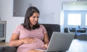 a woman in casual clothes smiling looking down at a laptop