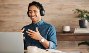 a man in casual clothes smiling with a headset on talking with his hands into a laptop