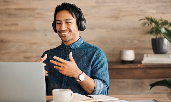 a man in casual clothes smiling with a headset on talking with his hands into a laptop