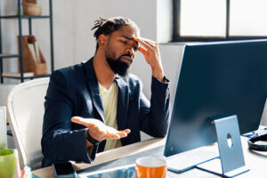 A man sitting down at a desk looking confused at his computer